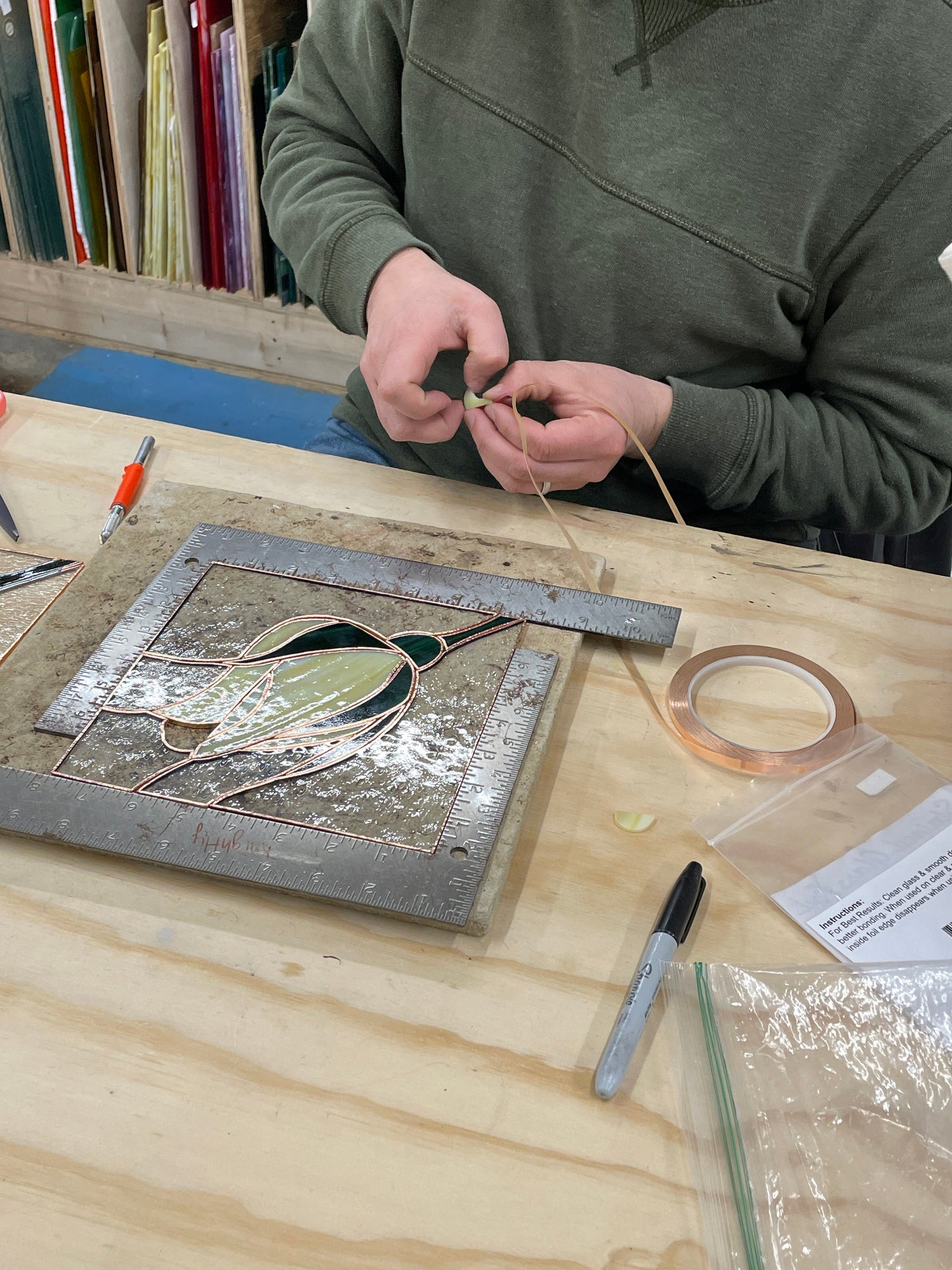 Stained glass student applying copper foil tape to glass pieces during a beginner class