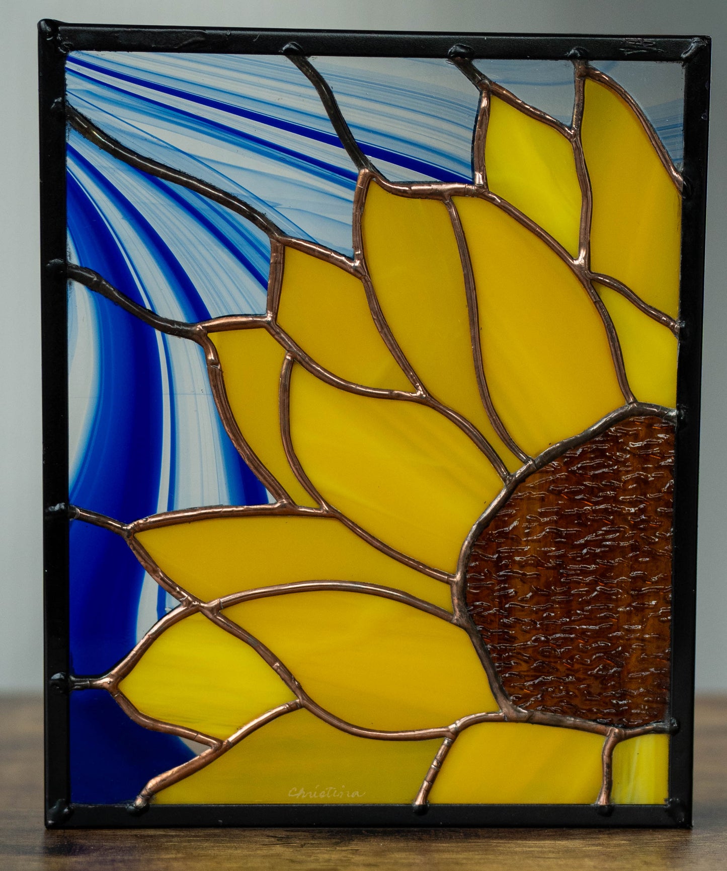 Stained glass sunflower artwork with blue and white abstract design in the background