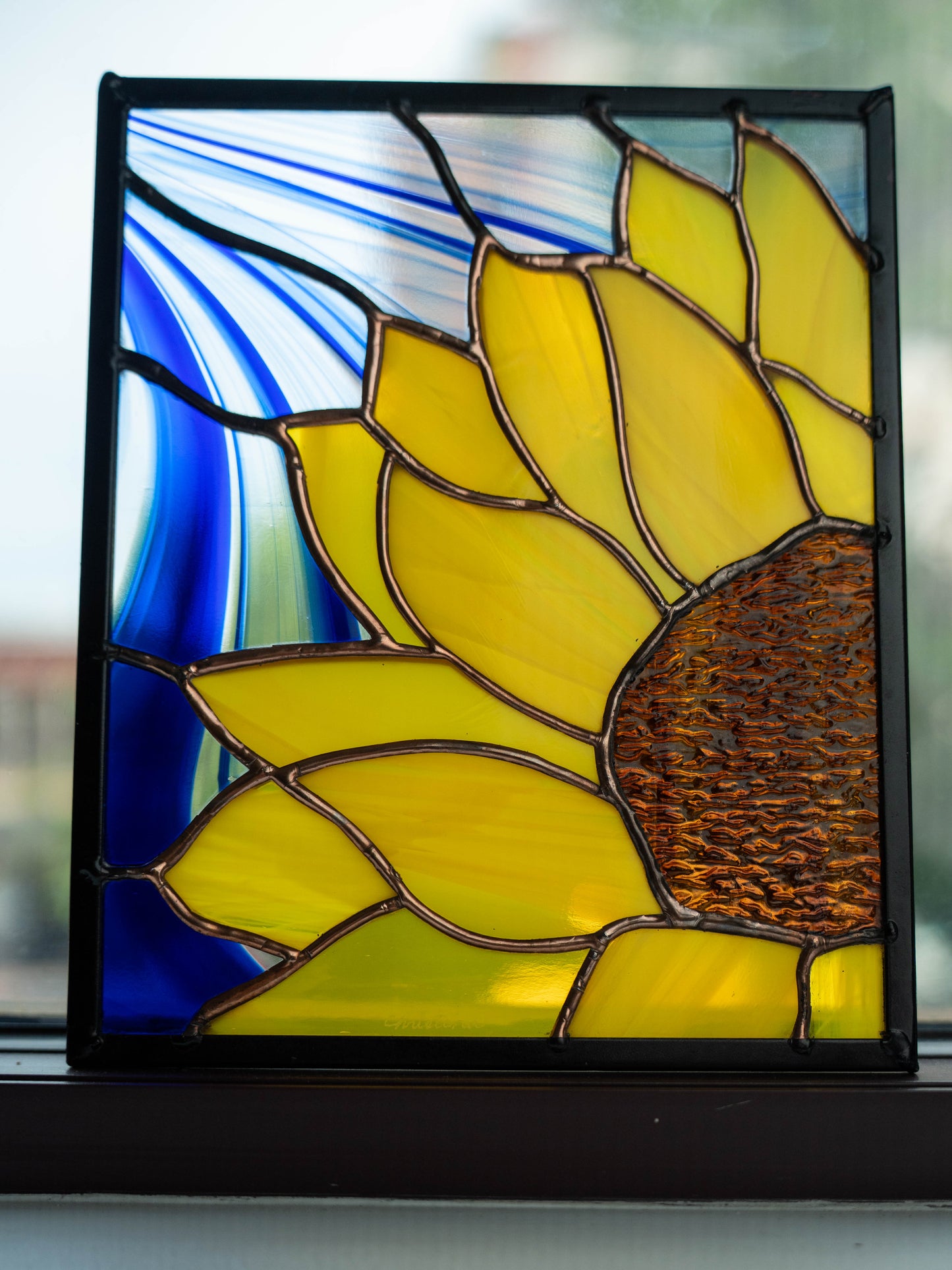 Stained glass panel of a sunflower with blue background